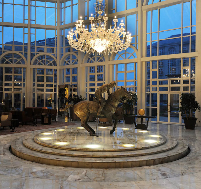 A chandelier above a statue of a person on a horse playing polo.